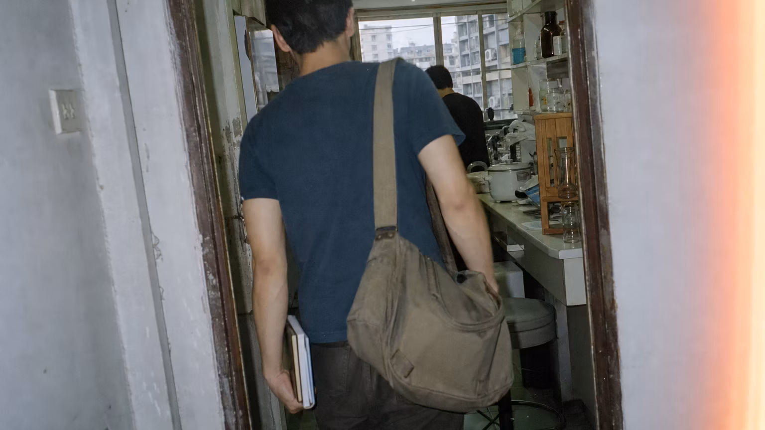 Grainy amateur-film image of an anonymous collaborator entering a modest Bangkok laboratory.