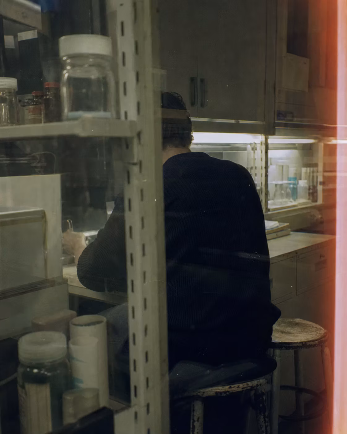 Underexposed amateur-film image of an anonymous collaborator seen through laboratory shelving.